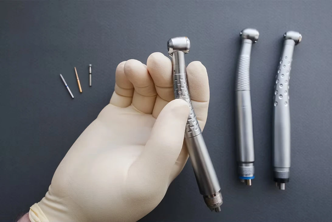 Gloved hand holding a dental handpiece alongside other handpieces